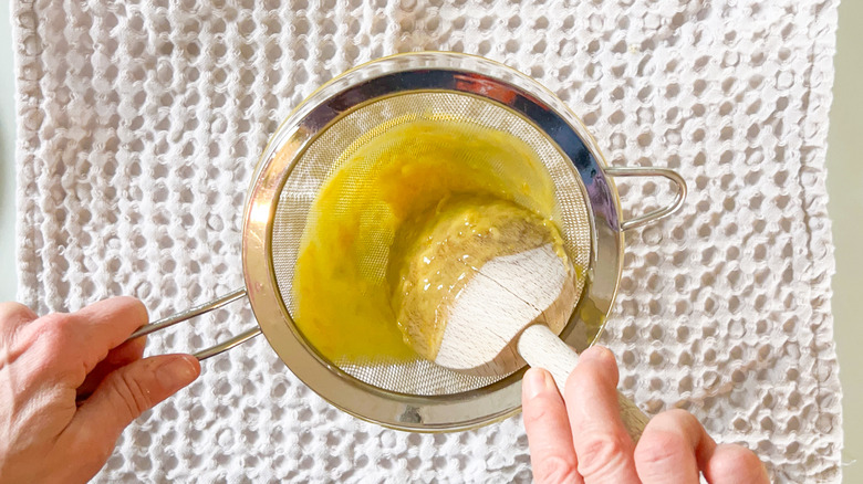 Straining lemon curd through colander into bowl with wooden spoon over towel