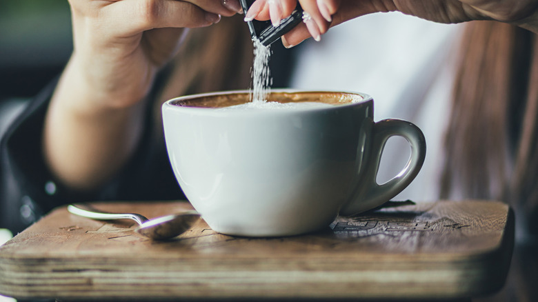 Person pouring sugar into coffee