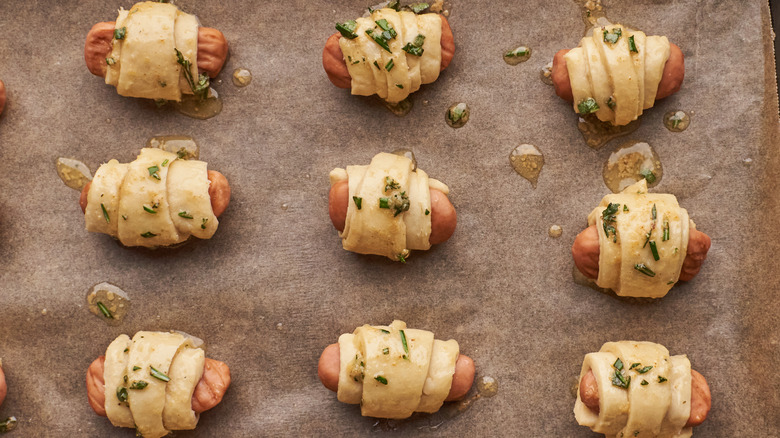 Uncooked herby pigs in a blanket on a baking sheet