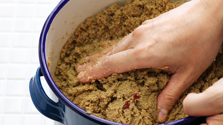 Hand mixing rice bran with brine and seasoning in a pot