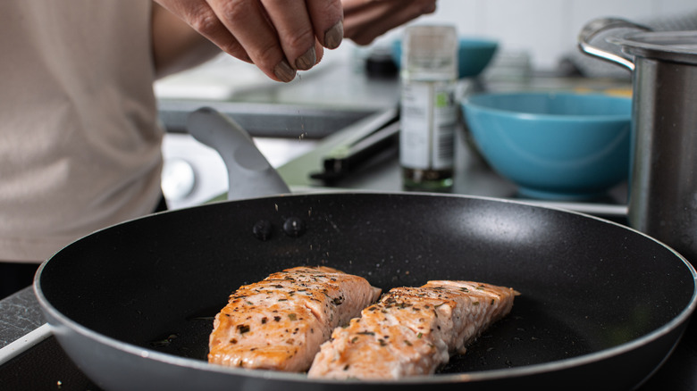 Hand seasoning fish in pan