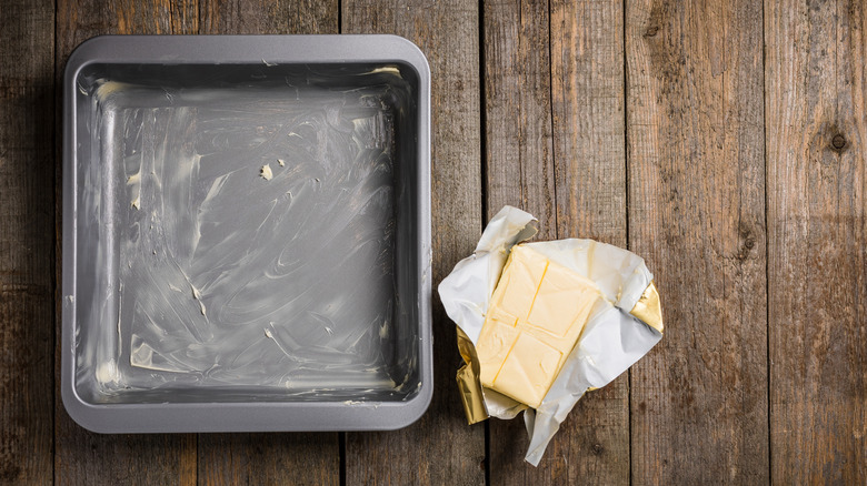 A square baking tin coated in butter with butter on the side