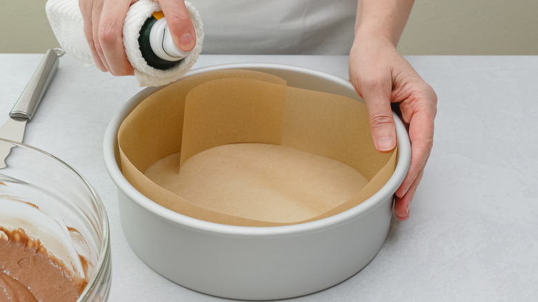 A cake tin with parchment paper being sprayed