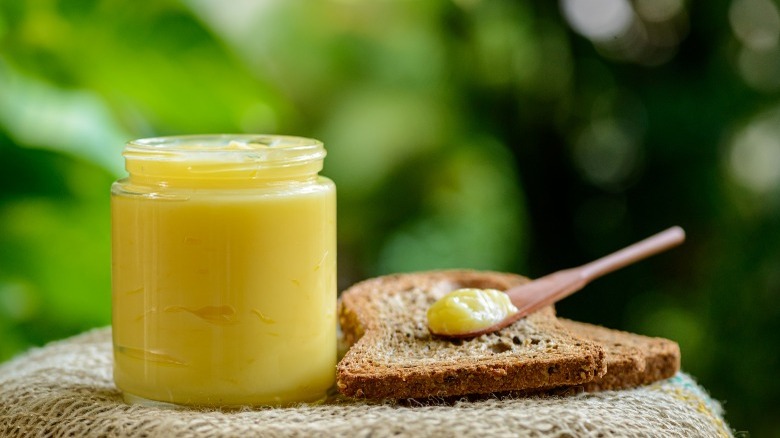 An open jar of ghee with bread and a wooden spoon in nature