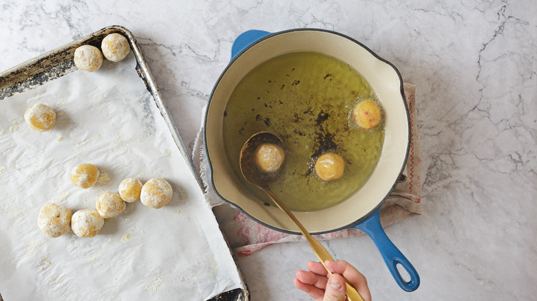 Hand using ladle to fry kofta in oil