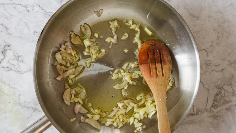 Shallots and garlic sauteing in oil with slotted wooden spoon