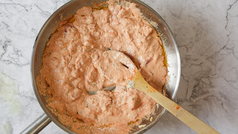 light pink sauce in a metal pan with wooden spoon