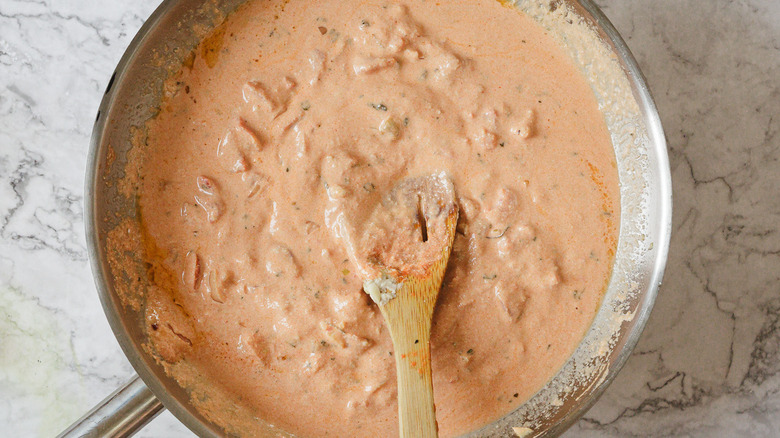 Wooden spoon and light pink sauce in pan