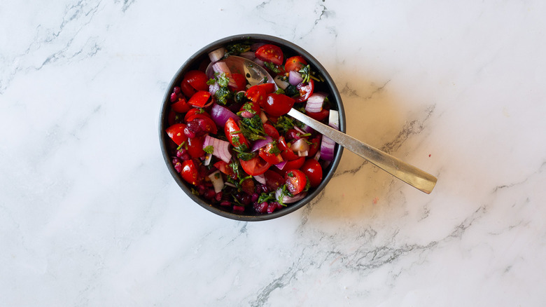 pomegranate, cherry tomatoes, onions and cilantro in bowl with spoon