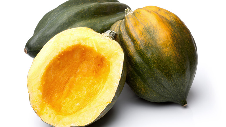A slice acorn squash next to two whole squash on a white background