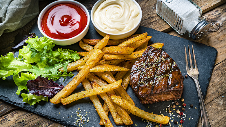 platter of grilled steak and fries with sauces and side salad