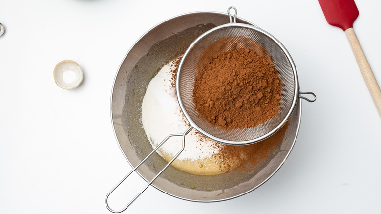 sifting cocoa powder into batter