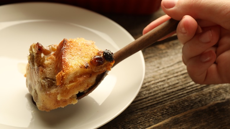 Someone scooping bread pudding onto a white plate