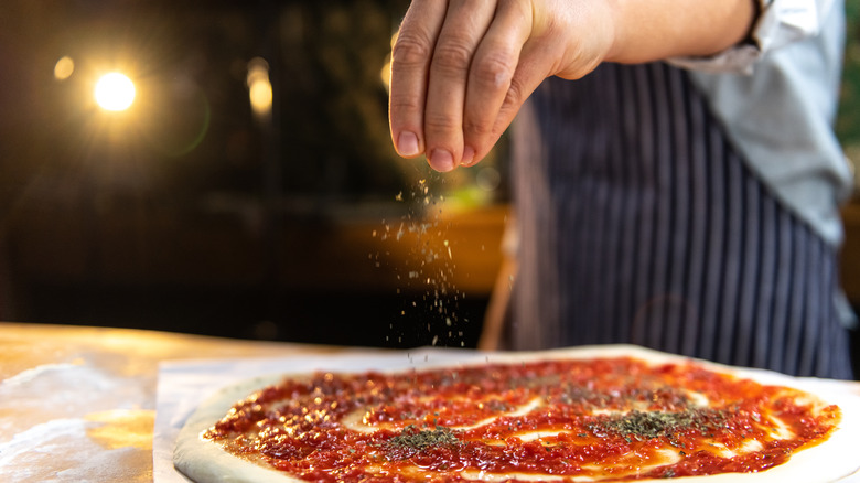 hand sprinkling oregano on pizza