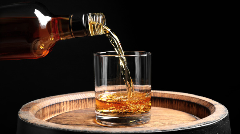 pouring bourbon in a glass on top of a barrel