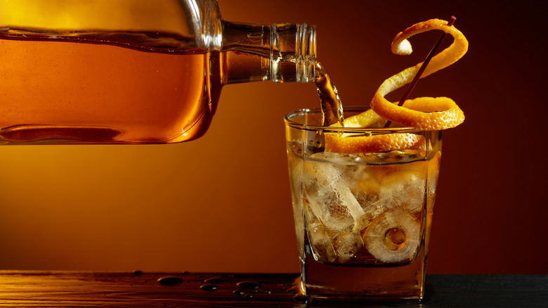 Pouring bourbon into glass with ice and orange peel