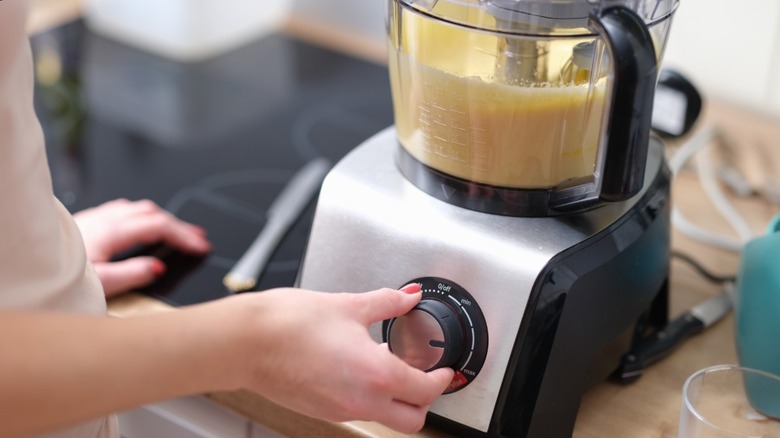 person turning knob on food processor containing cake batter