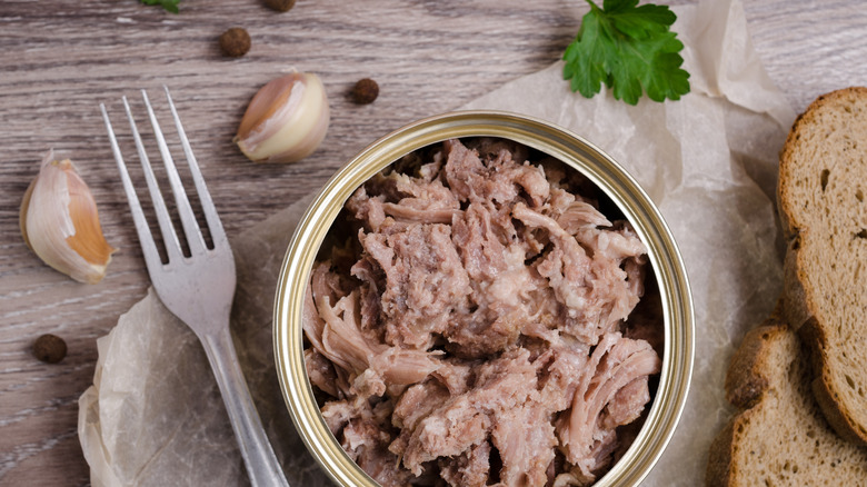 Canned meat, a fork, bread slices, and garlic cloves