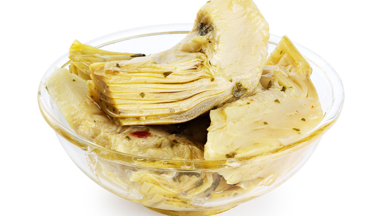 Glass bowl with canned artichokes on white background