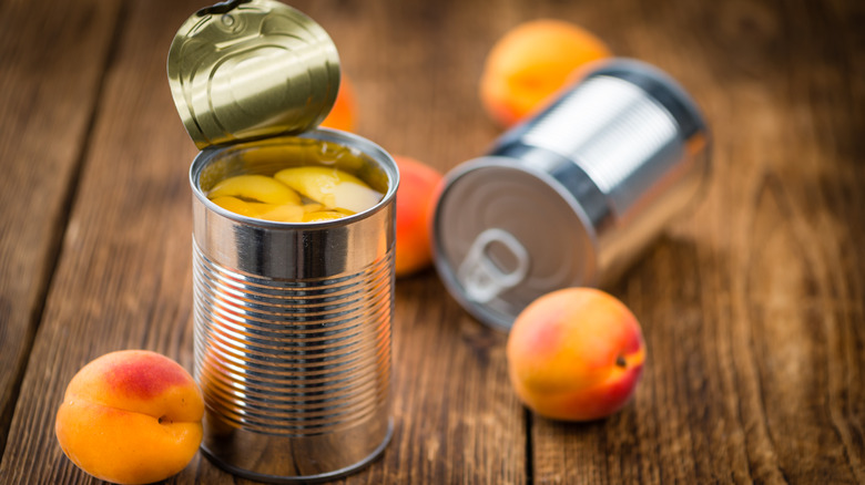 Open can of peaches beside fresh peaches