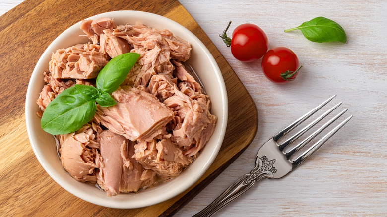 canned tuna in a bowl, topped with basil, alongside a fork and two cherry tomatoes