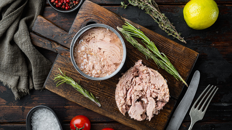 Tuna in and out of can on cutting board with herbs and spices