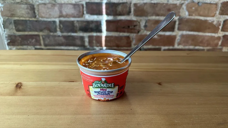 An opened can of Chef Boyardee mini spaghetti rings and meatballs with a spoon in it