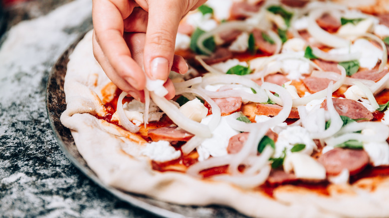 Hand putting onion on pizza 