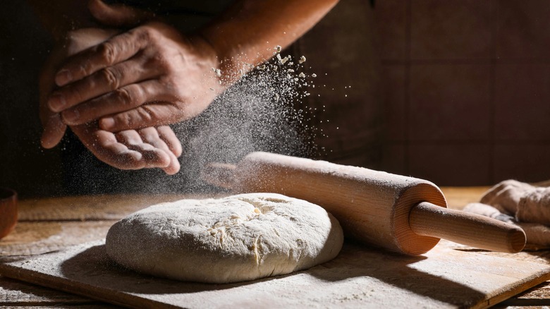 Person sprinkling flour on dough