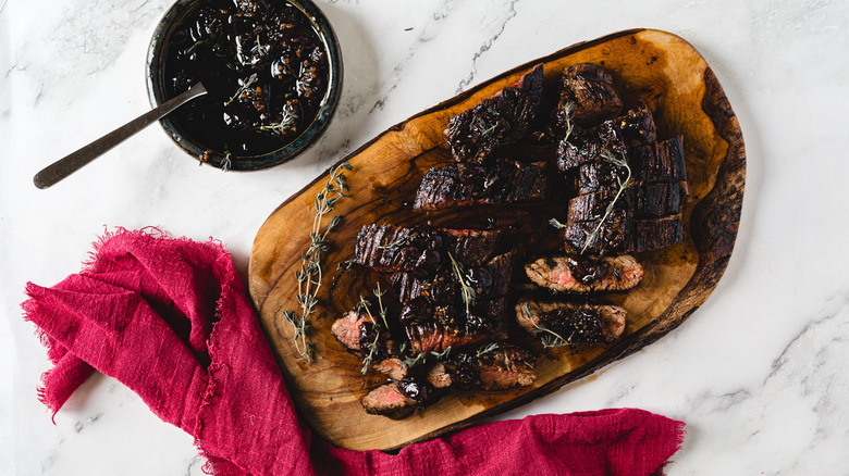 Sliced steak on cutting board besides cherry sauce