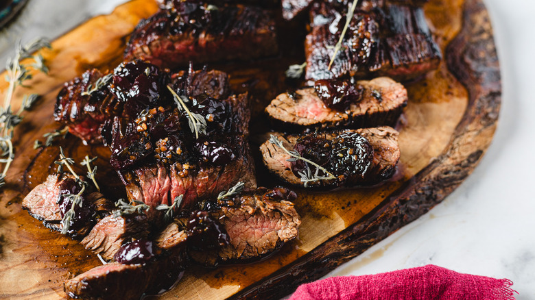 steak slices on a cutting board with cherry sauce in background