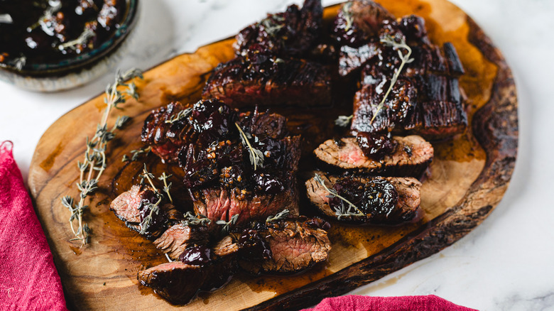 steak slices on a cutting board with cherry sauce in background