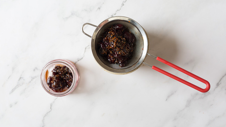 Strained cherries in colander besides jar with sauce