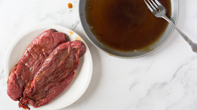 Steak in white plate besides marinade