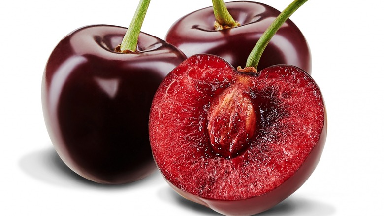 Two whole cherries and one sliced open showing pit on white background