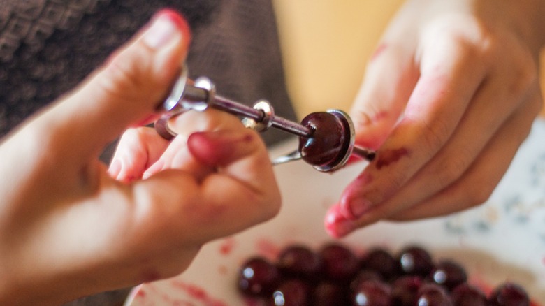 Hands pitting a cherry using a metal tool