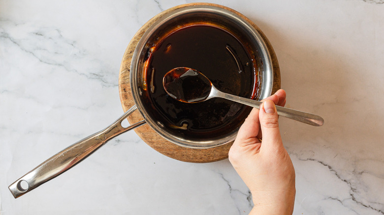 Hand lifting a spoon with balsamic reduction from saucepan