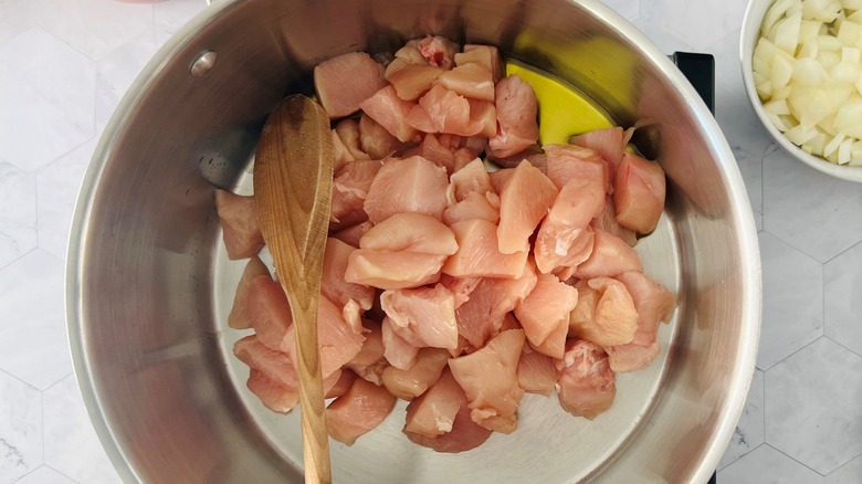 raw chicken cubes in pot with oil