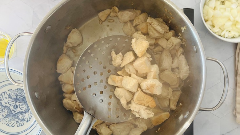 spoon removing browned chicken from pot