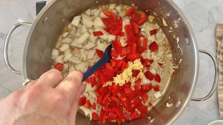 hand stirring diced vegetables in pot