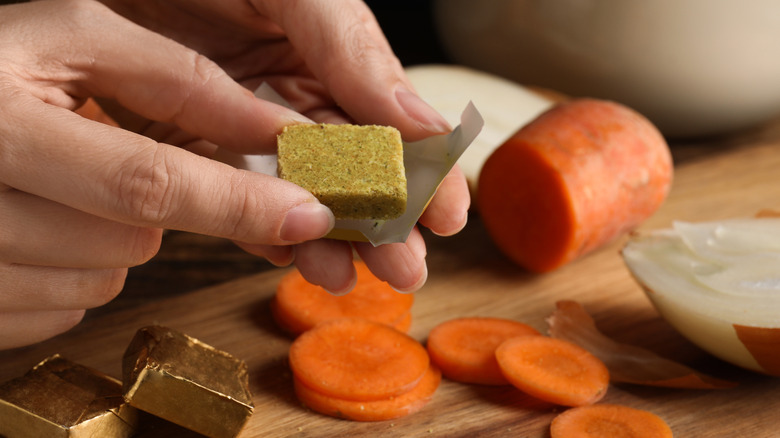 Person holding bouillon cube with other ingredients nearby