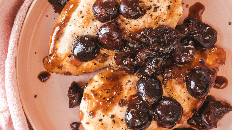 Two chicken breasts with cherry sauce on pink plate