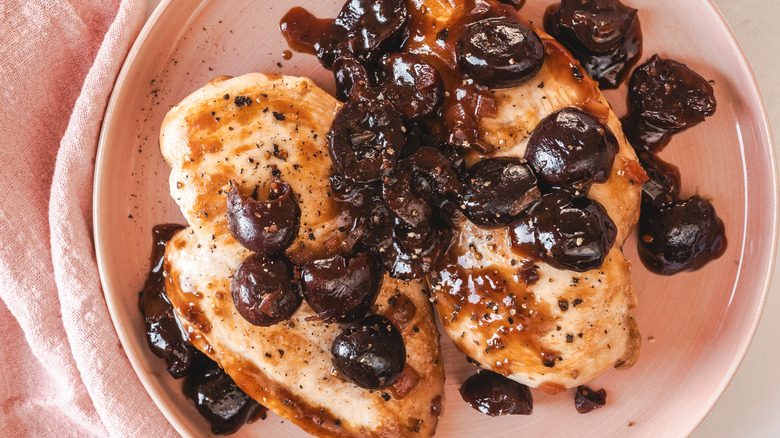 Two chicken breasts with cherry sauce on pink plate