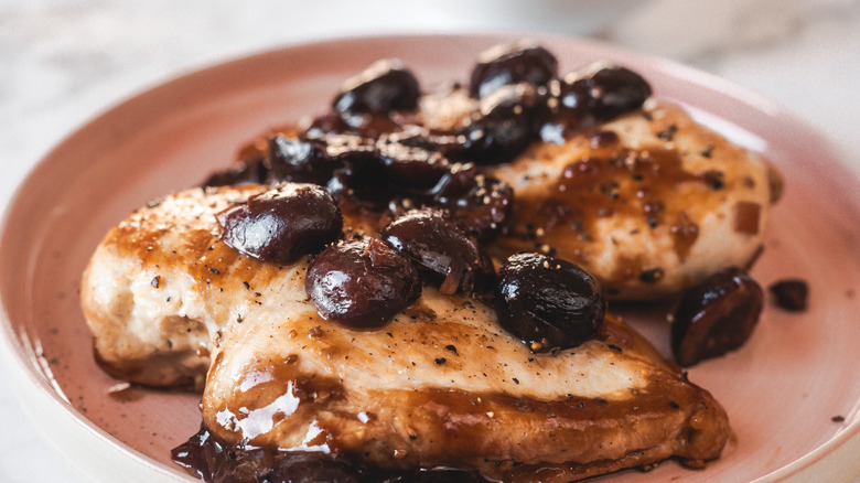 Two chicken breasts with cherry sauce on pink plate