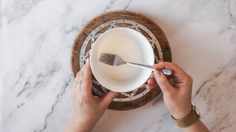 Hands mixing cornstarch and water with a fork in a bowl