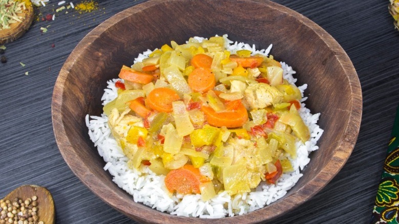 Chicken yassa with carrots on rice served in a wooden bowl