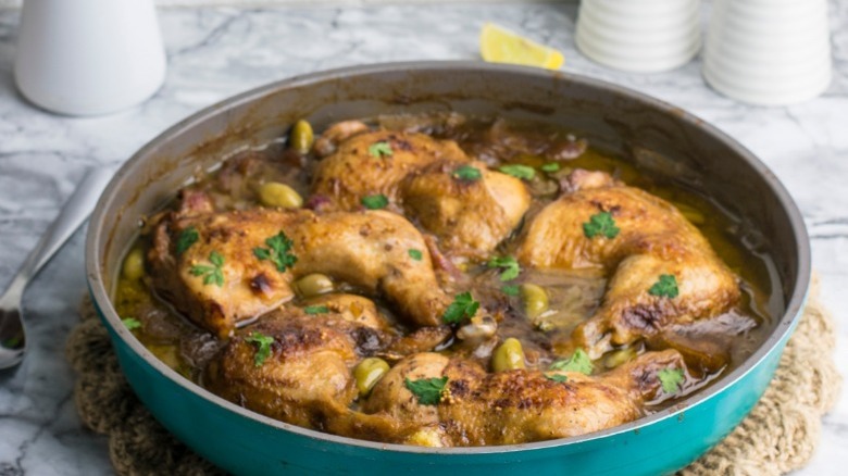 Fresh made chicken yassa sits in a pan top with parsley and olives