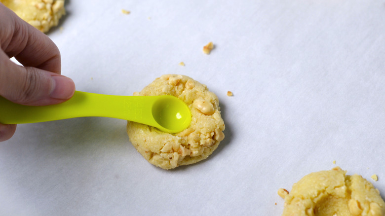 Pressing an indent into hazelnut thumbprint cookie dough with a measuring spoon