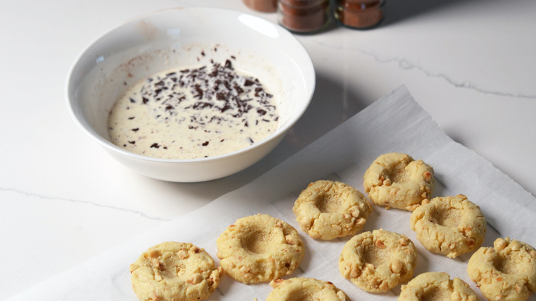 Thumbprint of cookies on a cooling rack with bowl of chocolate and cream in the background
