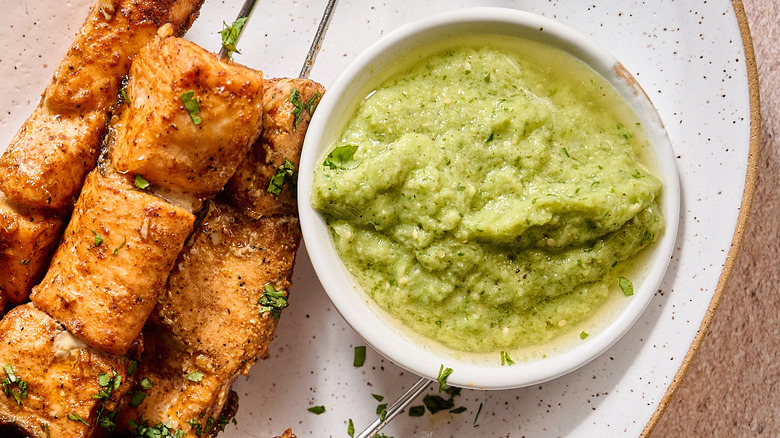 salmon skewers on a plate with bowl of salsa verde